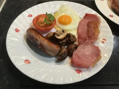 a plate of food with sausage eggs mushrooms and tomatoes at Sayang House in Church Stretton