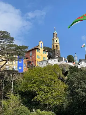 a group of buildings on a hill with a clock tower at Bron Eryri - Our Cosy House opposite the entrance to Portmeirion! in Mynfford
