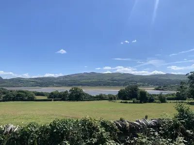 a field with a view of a river and mountains at Bron Eryri - Our Cosy House opposite the entrance to Portmeirion! in Mynfford