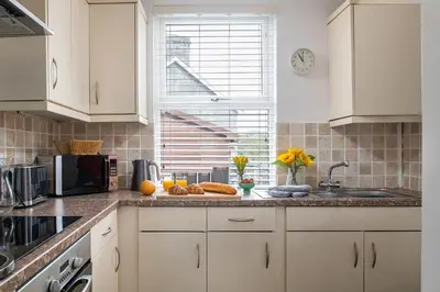 a kitchen with white cabinets and a counter with fruit on it at Bron Eryri - Our Cosy House opposite the entrance to Portmeirion! in Mynfford