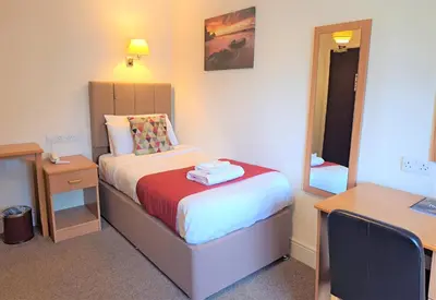 a small bedroom with a bed and a mirror at Richmond Hotel in Aberystwyth