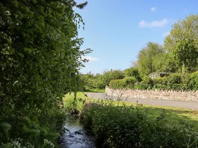 a river with a stone wall next to a road at Mucklewick Hollow in Shrewsbury