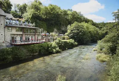 a river next to a building with people on a bridge at The Cart Shed Shropshire in Downton