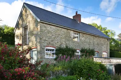 a brick house with a black roof and some flowers at The Groom's Flat in Leominster