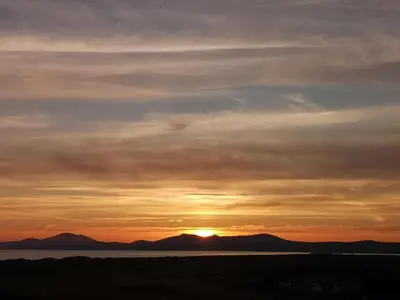 a sunset over the water with mountains in the background at Y Bwthyn in Llanbedr