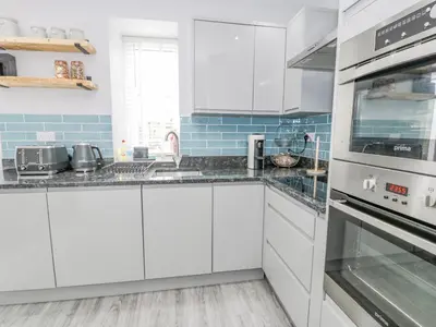 a white kitchen with white cabinets and blue tiles at Y Bwthyn in Llanbedr