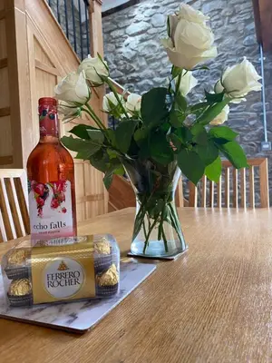 a vase with white roses and a bottle of beer at Pippin Lodge in Llanwrda