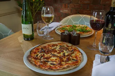 a wooden table with two pizzas and wine glasses at The Wynnstay Hotel, Oswestry, Shropshire - The Coaching Inn Group in Oswestry