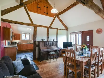 a living room with a table and a kitchen with a piano at Y Dderwen in Pen-y-bont-fawr