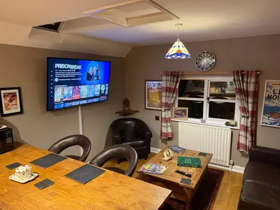 a dining room with a table and a flat screen tv at Bear Cottage, Tyn Y Cwm in Scyborycoed
