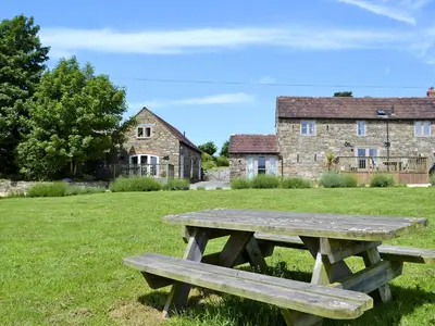 a wooden picnic table in a field with buildings in the background at St Vincent in Plaish