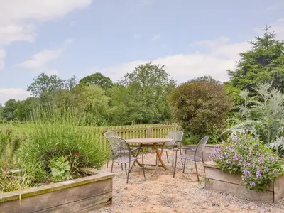 a patio with chairs and a table in a garden at Stoke Court Farm Barn in Stoke Saint Milborough