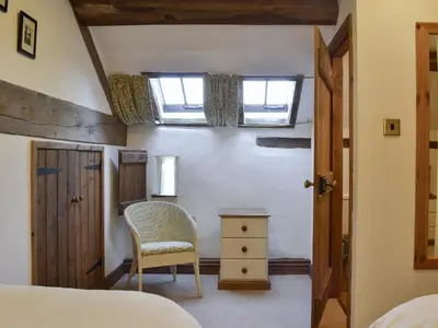 a bedroom with a bed and a chair and a window at Oak Barn Cottage in Trefonen