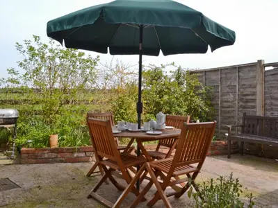 a table and chairs with a green umbrella at Honeysuckle Cottage in Minsterley