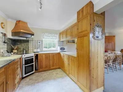 a kitchen with wooden cabinets and a dining room at Walnut Tree Cottage in Bucknell