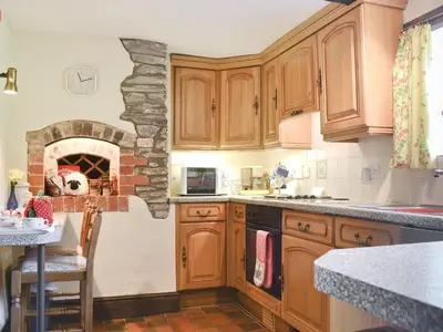 a kitchen with wooden cabinets and a stone fireplace at Forget Me Not Cottage in New Radnor