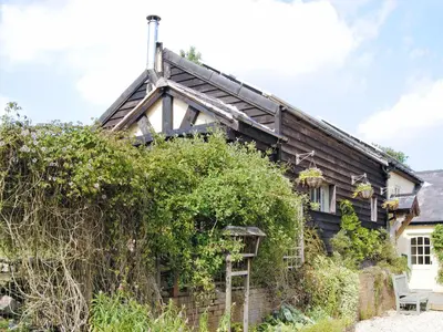 a wooden house with ivy on the side of it at Hirros Hall Longhouse in Llanerfyl