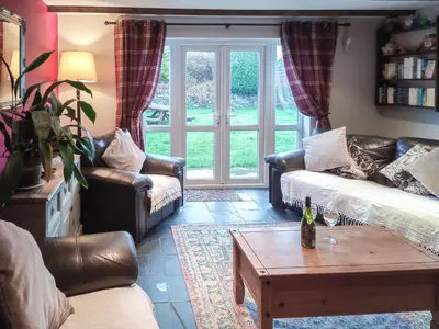 a living room with a couch and a table with a bottle of wine at Panteg Cottage in Cross Inn