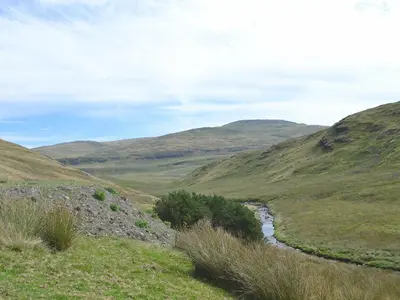 a river in a field with hills in the background at Llechwedd Mawr in Scyborycoed