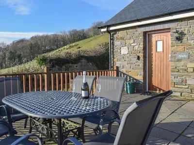 a table and chairs on a deck with a bottle of wine at Beudy-Oh2 in Dihewid