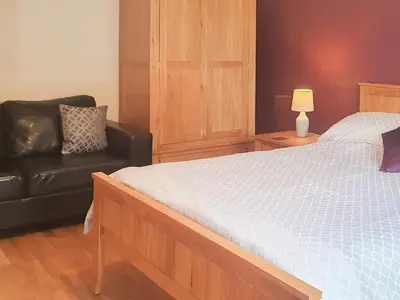 a bedroom with a bed and a black leather couch at Beudy Bach-Oh5 in Dihewid