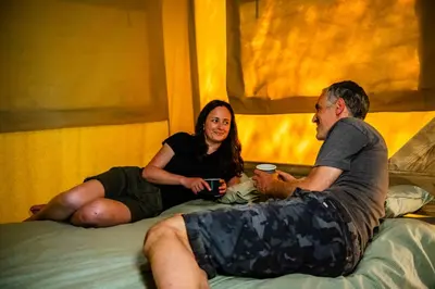 a man and a woman sitting on a bed at Luxury Safari Tent with Hot Tub in Ancient Woodland in Acton Scott