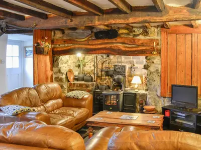 a living room with leather furniture and a stone wall at Hen Hafod in Llanfor