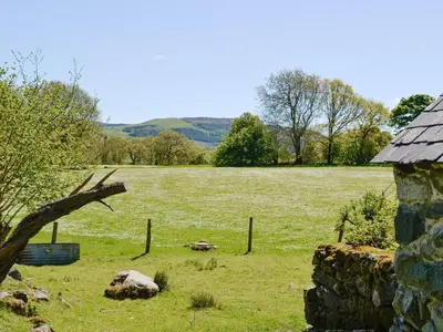a field of grass with a fence and a stone building at Hen Hafod in Llanfor