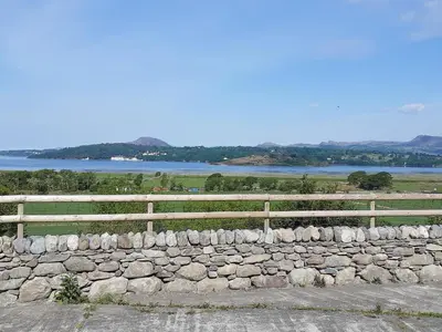 a stone wall with a fence and a lake at The Barn in Talsarnau
