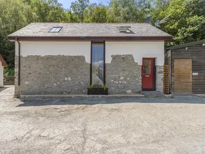 an old brick building with a red door at Y Beudy in Capel Bangor