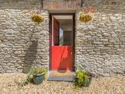 a stone building with a red door and potted plants at Y Beudy in Capel Bangor