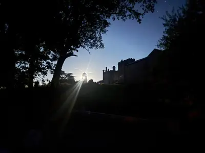 a sun setting behind a house with a tree at Llanerchydol Hall Suites in Welshpool