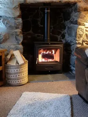 a stone fireplace with a stove in a room at Glasfor Cottage in Llwyngwril