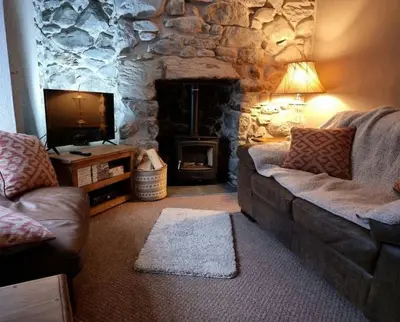 a living room with a couch and a stone fireplace at Glasfor Cottage in Llwyngwril