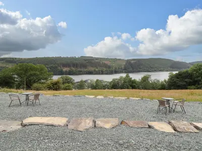 a group of tables and chairs on a gravel area with a lake at Hen Blaid in Oswestry