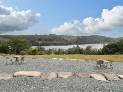 a group of tables and chairs on a gravel area with a lake at Llety Dewi in Oswestry