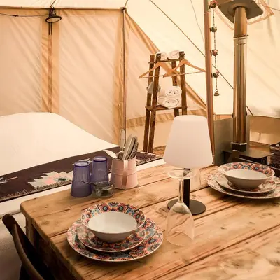 a wooden table with two plates and a lamp on it at Tinker the Bell Tent at Pentref Luxury Camping in Penuwch