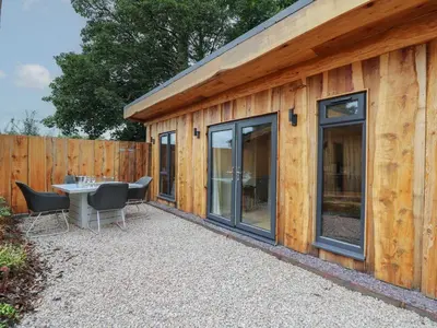 a patio with a table and chairs next to a wooden building at Rhosyn in Welshpool