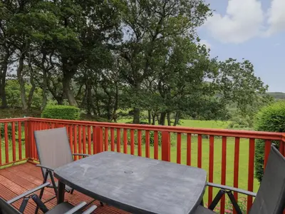 a table and chairs on a deck with a fence at Chalet 64 in Tywyn