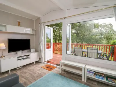 a living room with a television and a balcony at Chalet 64 in Tywyn