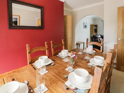 a dining room with a table and chairs and a red wall at 24 Dolithel in Tywyn