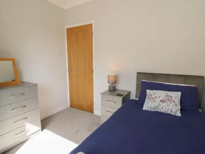 a bedroom with a blue bed and a dresser and a mirror at 24 Dolithel in Tywyn