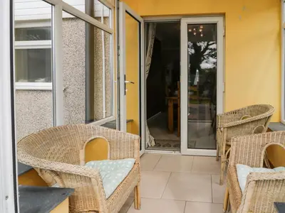 a patio with wicker chairs and an open door at 24 Dolithel in Tywyn