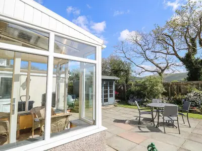 a conservatory with glass doors and a table and chairs at 24 Dolithel in Tywyn