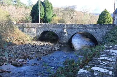 an old stone bridge over a river in a field at Dolafon in Llanbedr