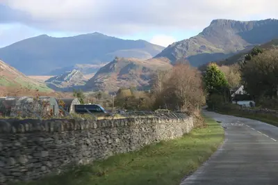 a stone wall next to a road with mountains at Dolafon in Llanbedr