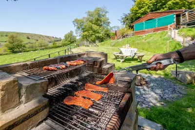 a person is cooking hot dogs on a grill at Ty Grug Pods in Bryngwyn