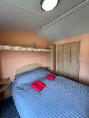 a bedroom with a blue bed with two red pillows at Light and Airy 2 Bedroom Mobile Home in Aberystwyth