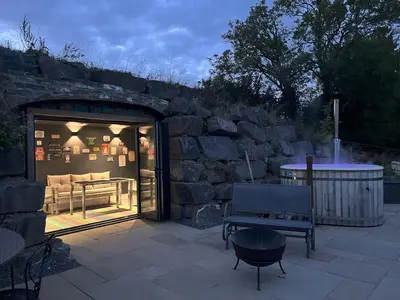 a patio with a stone wall and a table and a bench at Honeybee Home in Llansantffraid-ym-Mechain