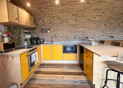 a kitchen with yellow cabinets and a brick wall at Honeybee Home in Llansantffraid-ym-Mechain